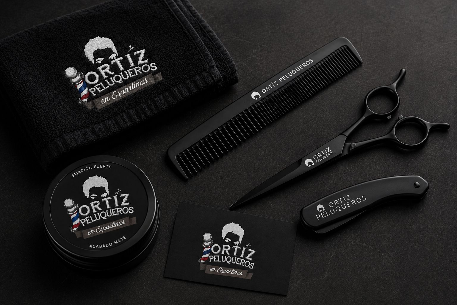 Toalla bordada, peine, tijeras, navaja y lata de cera de fijación fuerte de Ortiz Peluqueros, todos en negro